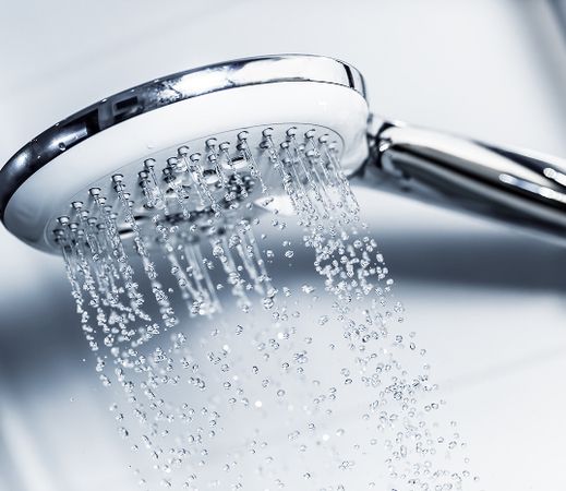 Nahaufnahme eines modernen Duschkopfs mit herabfallenden Wassertropfen vor einem hellen, gefliesten Hintergrund.