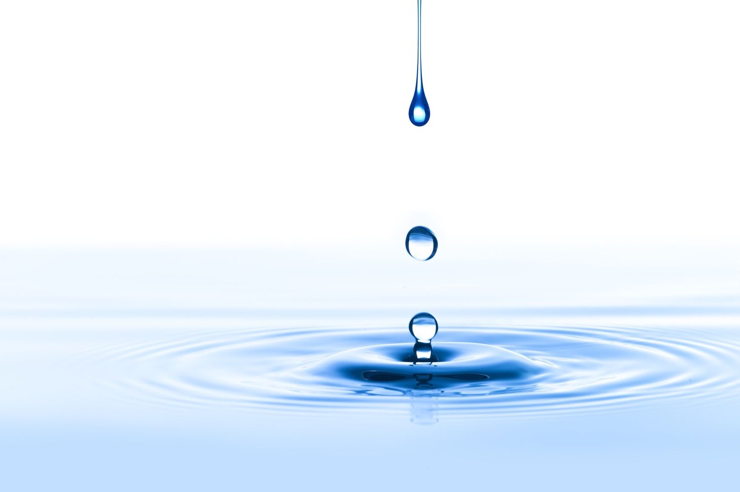 Ein Wassertropfen fällt von oben und erzeugt Wellen auf einer ruhigen blauen Oberfläche, wodurch die Essenz von Ruhe und Flüssigkeit eingefangen wird.